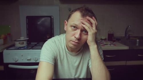 Man Sits Thoughtfully in Gloomy Kitchen