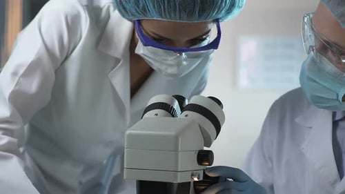 Scientist and Lab Assistant Looking Into Microscope at Reaction of Samples