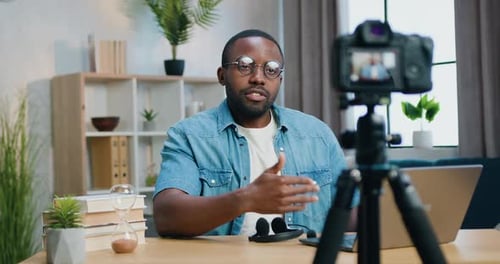 Bloguero afroamericano con gafas grabando un Vídeo ante la cámara para su audiencia de Internet