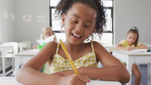 Video of happy biracial girl sitting at school desk and learning
