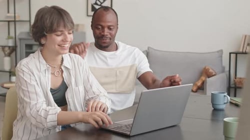 Pareja multiétnica viendo videos en el portátil y bailando en casa