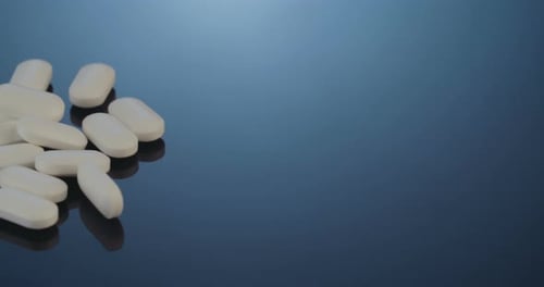 Oval White Pills Falling on Reflective Blue Surface