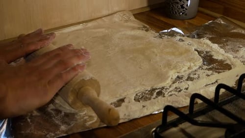 Amateur pizza maker stretching the pizza dough using wooden rolling pin in domestic kitchen. Home co