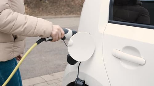Woman Coming to the Electric Vehicle and Plugging in Power Supply Cable to Charge in the Street at