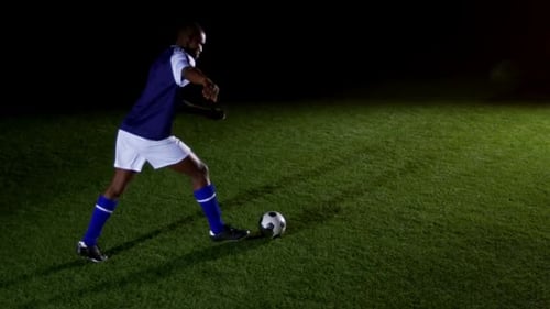 Soccer Player Kicks Ball on Grassy Field at Night