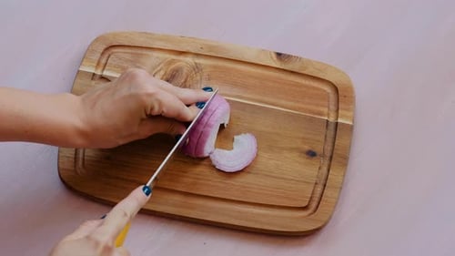 Top view of woman hands with knife cutting onion for salad on a wooden board