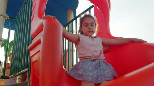 Cute Little Girl Slides Down the Slide at the Playground in Summer