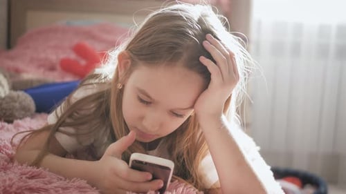 Child Uses Smartphone While Lying in Bed