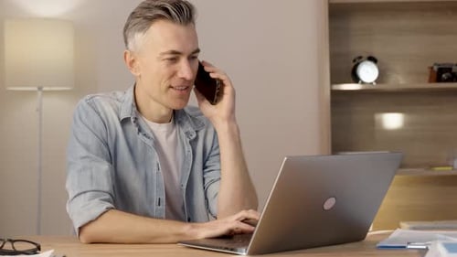 Man Talking on Smartphone While Working on Laptop