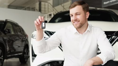 A Man with Keys Rejoices in Buying a New Electric Car in a Car Dealership