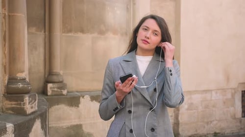 Caucasian Attractive Businesswoman Putting on Headphones Earphones on the Street