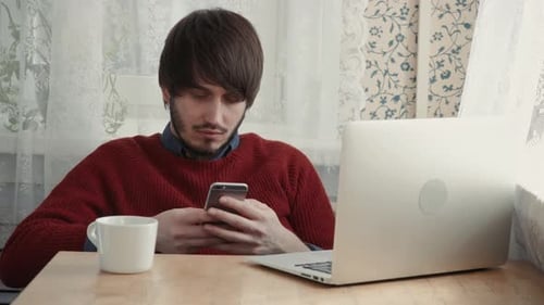 Young Male Freelancer Chatting on Mobile Phone While Sitting Front Open Laptop Computer Cafe