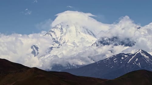 Timelapse Clouds Swirl Over a Mountain Valley a Snowy Peak in the Distance