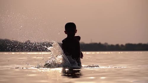 Boy Splashing in Water at Sunset