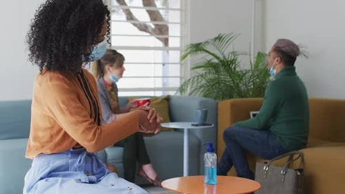 Woman wearing face mask sanitizing her hands at office