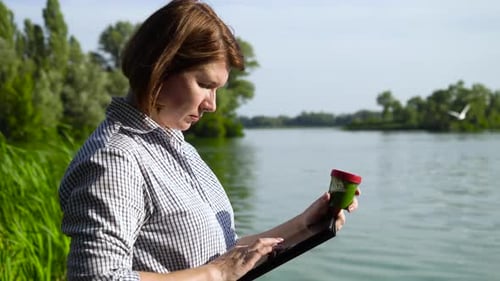 side view of ecologist examining green algae sample and entering data on tablet