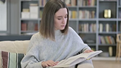 Young Woman Reading a Book Indoors on Sofa