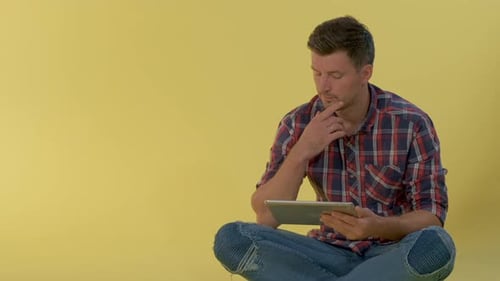 Close-up of Intelligent Young Man Working on Tablet on Yellow Background.