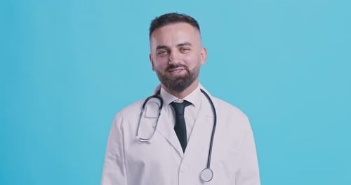 Friendly Middle Aged Doctor Nodding Head Yes and Smiling at Camera, Blue Studio Background