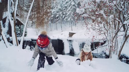 Glückliche Kinder in warmen Mänteln und Mützen werfen Schnee auf den verschneiten Hintergrund.