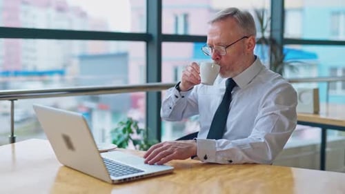 Man Using Laptop and Drinking Coffee at Office Desk