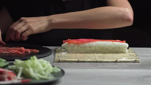 Woman Making Sushi Roll with Salmon and Cucumber