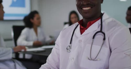 Porträt eines afroamerikanischen Arztes, der lächelnd im Besprechungsraum sitzt und in die Kamera blickt