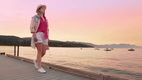 Cinematic Slow Motion of Woman Walking By Beach Pier with Pink Sky on Background