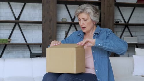 Senior Woman Opening Cardboard Box on Sofa