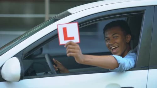 Smiling Boy Showing L-Plate at Car Window, Driving Courses, Right-Hand Traffic