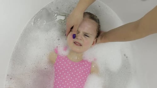 Nettes blondes Mädchen badet in Bademode. Kleines Kind wäscht den Kopf