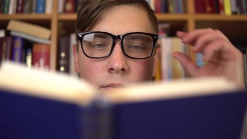 Ein junger Mann liest ein Buch in einer Bibliothek. Ein Mann mit Brille schaut sich das Buch sorgfältig an Nahaufnahme