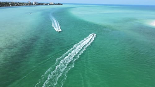 Camera is flying between boats as they cross paths near the opening of a small bay into the wide oce