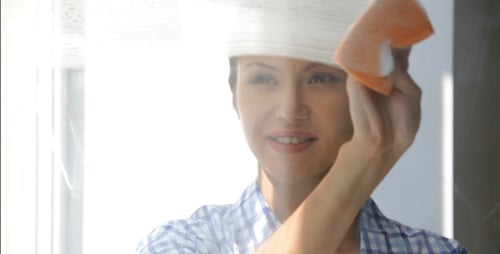 Woman Cleans Window with Squeegee in Bright Home