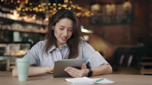Woman in Earphones Using Tablet While Resting at Cafe