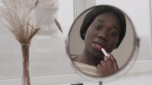 Reflection of Young African Woman Applying Lipstick