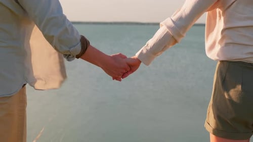 Couple Holding Hands Overlooking Lake On Sunny Day