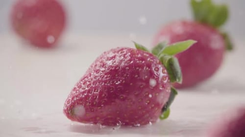 Erdbeere fällt mit Wassertropfen in Zeitlupe auf einen Haufen frischer Beeren