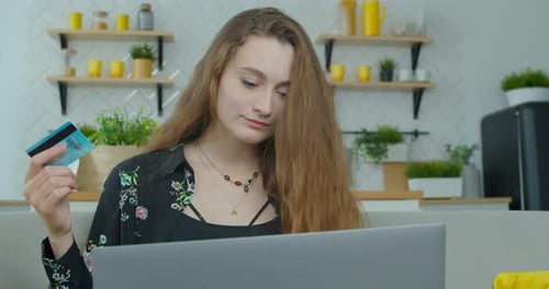 Young Woman Is Making Online Payment Holding Bank Card Using Modern Laptop at Home Sitting on Sofa