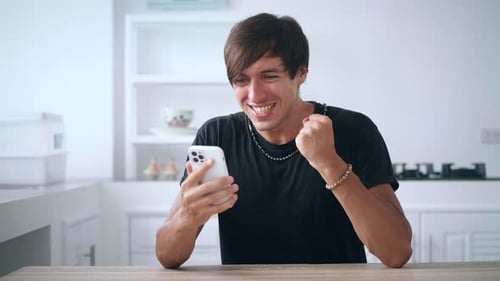 Man Reacts to Good News on Smartphone in Kitchen