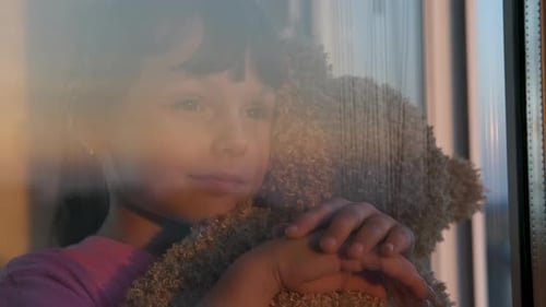 Child Hugging a Teddy Bear at a Window
