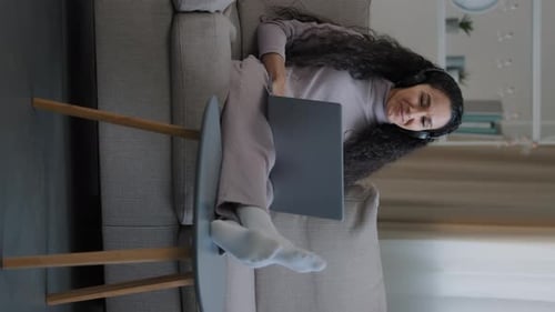 Vertical View Happy Young Arab Woman Girl with Curly Hairstyle Sit on Cozy Sofa Talk at Headset