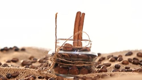 Little Bottle with Coffee Beans and Cinnamon on Sacking, Close Up, White Background