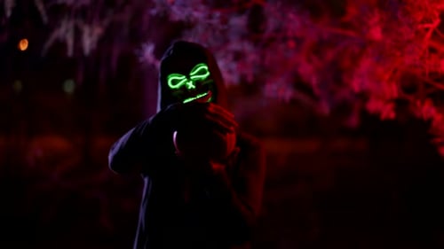 a Person in a Terrible Glowing Mask of Death and in a Cape with a Hood Stands with a Skull in Hands