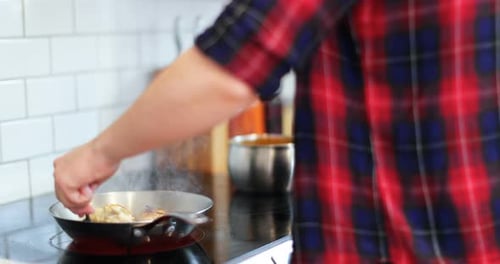 Person Cooking Food in Pan in Kitchen