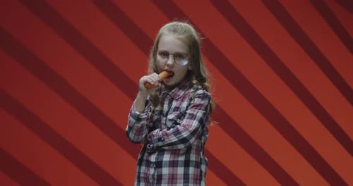 Girl Eating Carrot Against Red Background