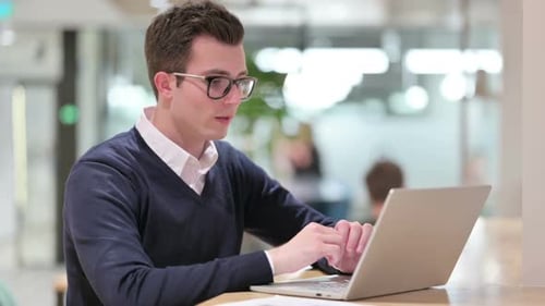 Young Adult Man Works on Laptop at Desk