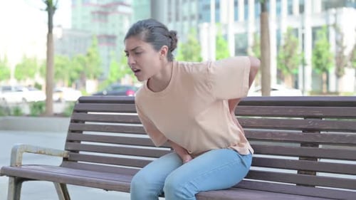 Woman Experiencing Back and Abdominal Pain on Bench
