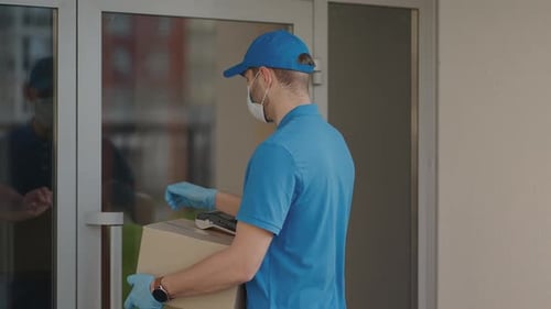 A Delivery Man Wearing a Protective Mask and Gloves Passes the Parcel to the Customer and Receives a