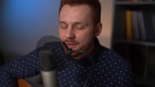 Man Singing and Playing Guitar into Microphone